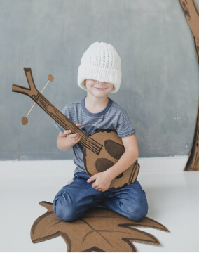 A young boy playing a cardboard guitar.