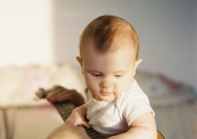 A baby sitting down being held by a parent.