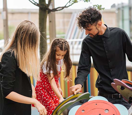 A man and woman joyfully engage with a child on a vibrant playground, surrounded by swings and slides.