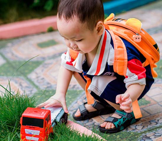 A young boy happily playing with a toy truck while wearing a backpack.