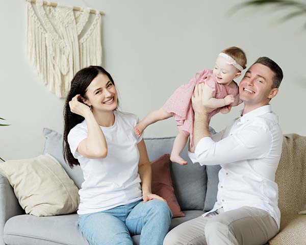 A man and woman sit together on a couch, gently cradling a baby between them, showcasing a moment of family bonding.