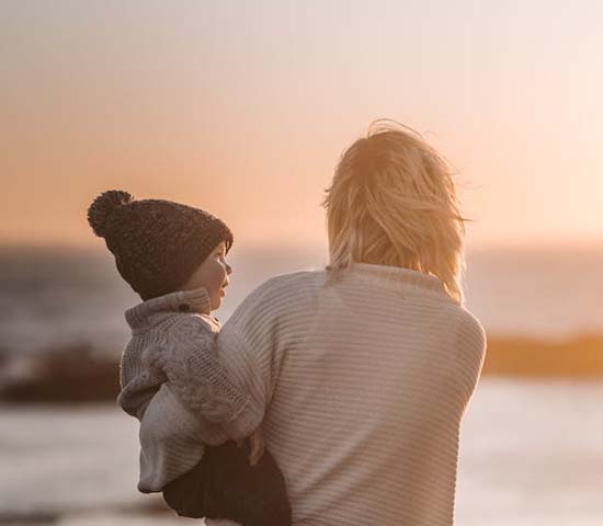 A woman holding a child on the beach at sunset.